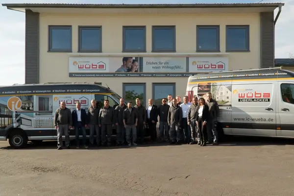 Mitarbeiter des Ideencenters Wüba stehen vor dem Firmengebäude und zwei Firmenfahrzeugen.