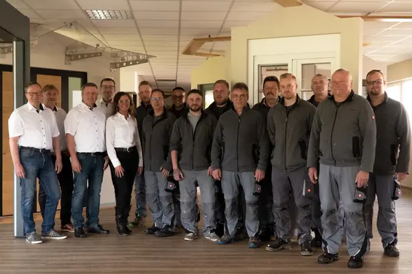 Gruppenfoto eines Handwerker- und Büroteams in moderner Firmenumgebung mit Holzarbeiten.