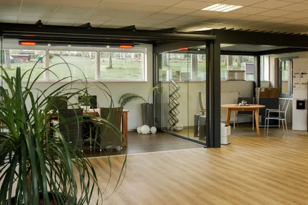 Modernes Büro mit Glaswänden, Holzboden, Pflanzen und großen Fenstern für Tageslicht.