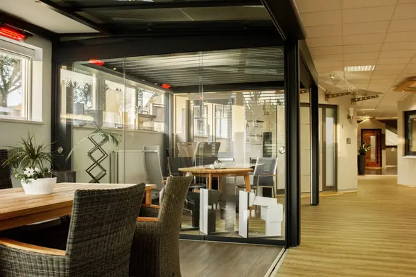 Moderner Ausstellungsraum mit Wintergarten, Glaswänden, Holztisch und Lounge-Möbeln.
